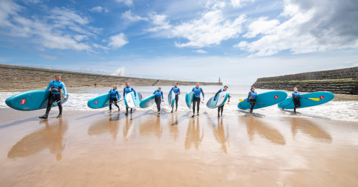 group of people walking out of sea holding paddleboards at Seaham Harbour Marina.